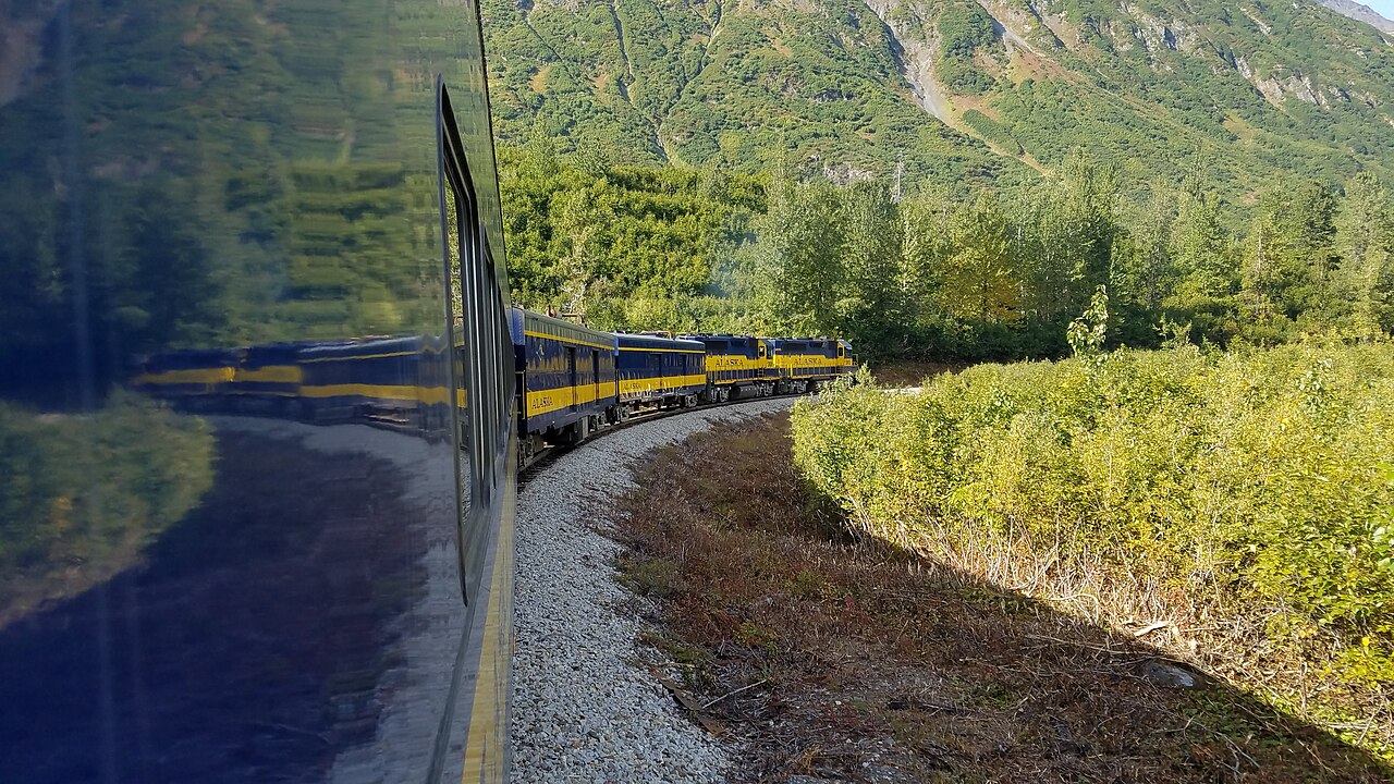 Blue-and-yellow Alaska Railroad Glacier Discovery Train rounding a mountain curve
