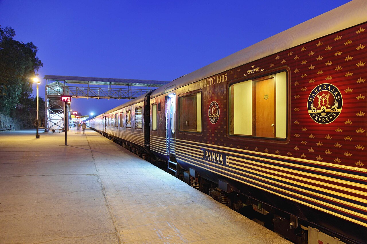 Illuminated red-and-gold Maharajas’ Express carriages beside a station platform