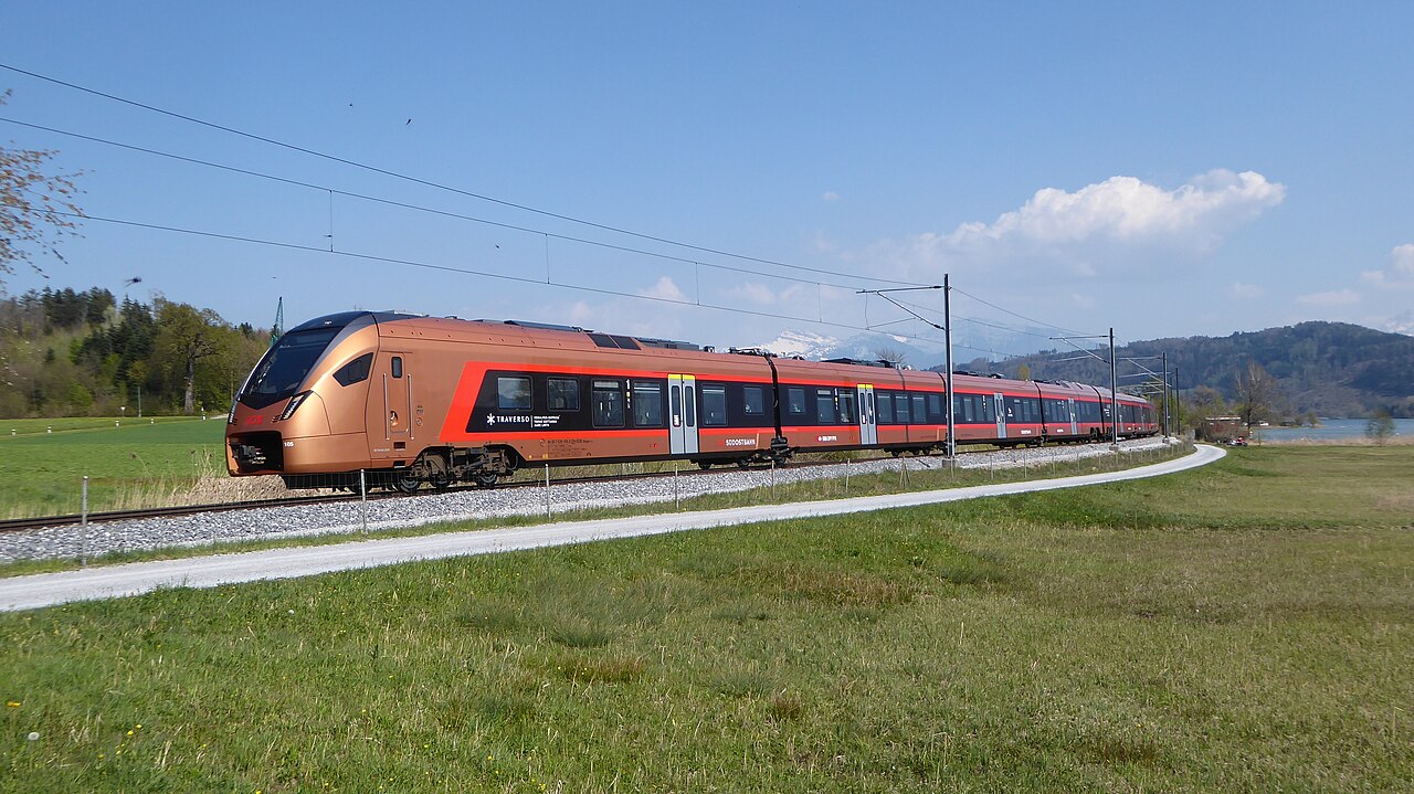 Copper-and-red Voralpen Express train beside green fields in Switzerland